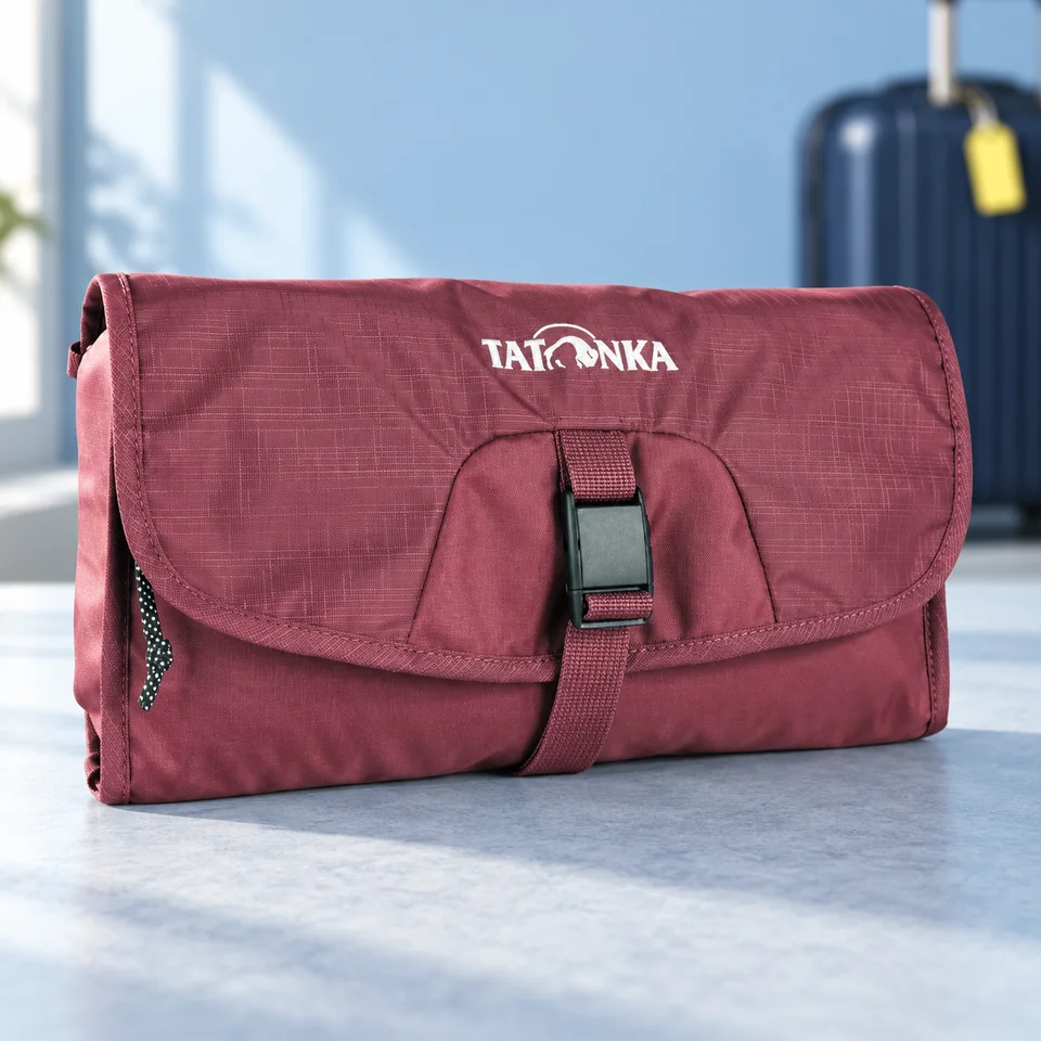 Tatonka — Small Travelcare bordeaux avec miroir de Tatonka, mise en situation dans un univers de voyage bleu-gris